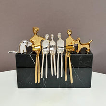 Load image into Gallery viewer, gold and silver sculptures of a family seated on a black marble stone.

