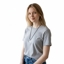 Load image into Gallery viewer, Yenny Cocq Design silver circular pendant necklace on a black cord, worn by a woman in a grey t-shirt.

